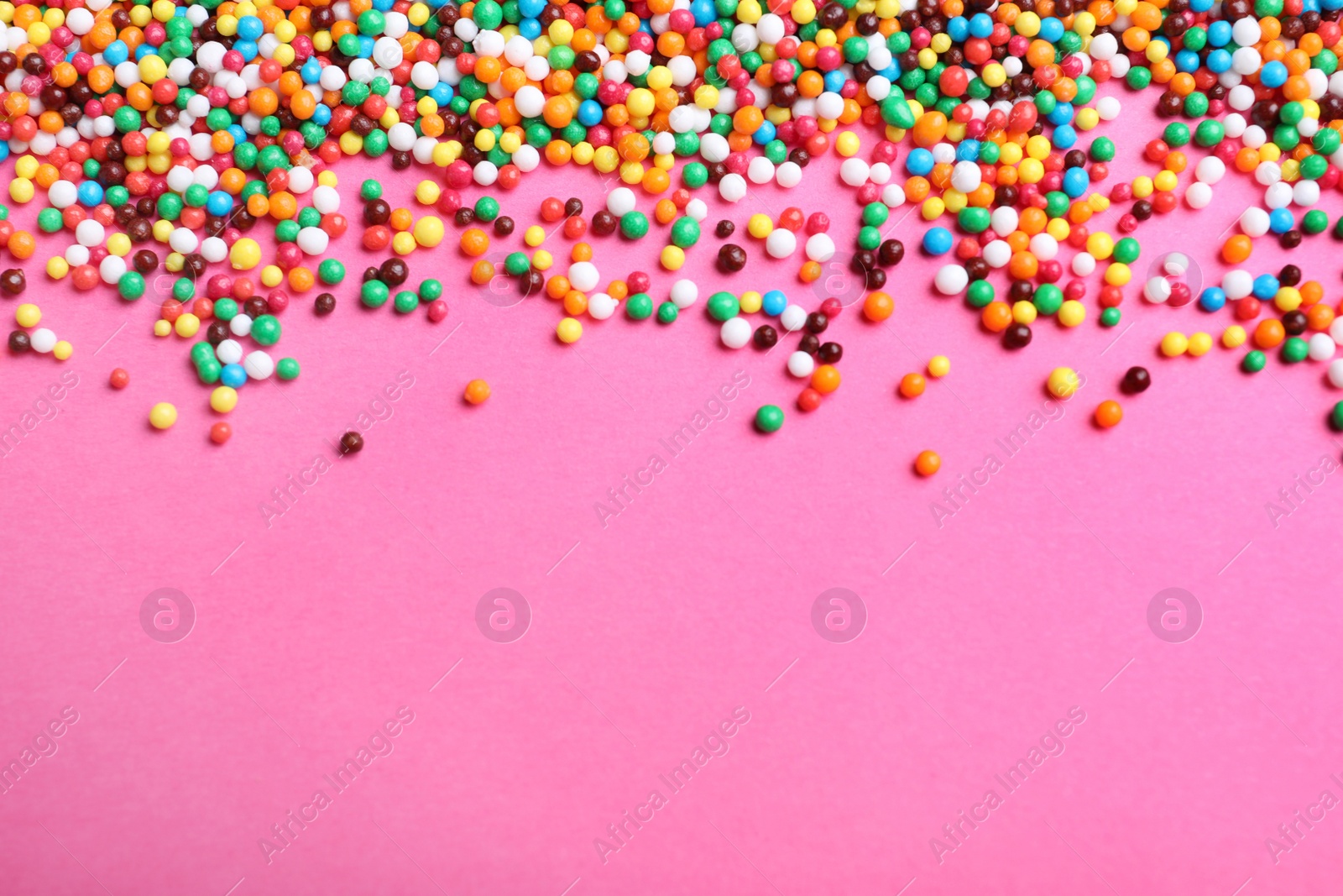 Photo of Bright colorful sprinkles on pink background, flat lay with space for text. Confectionery decor