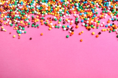 Photo of Bright colorful sprinkles on pink background, flat lay with space for text. Confectionery decor