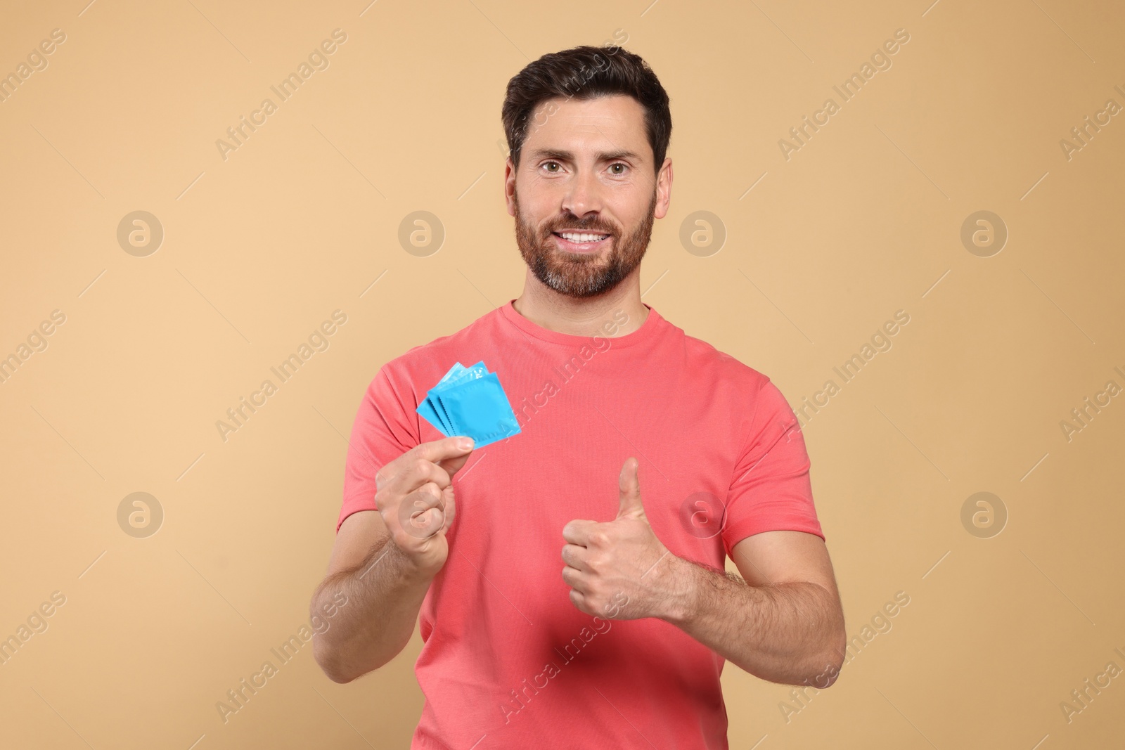 Photo of Happy man with condoms showing thumb up on beige background. Safe sex