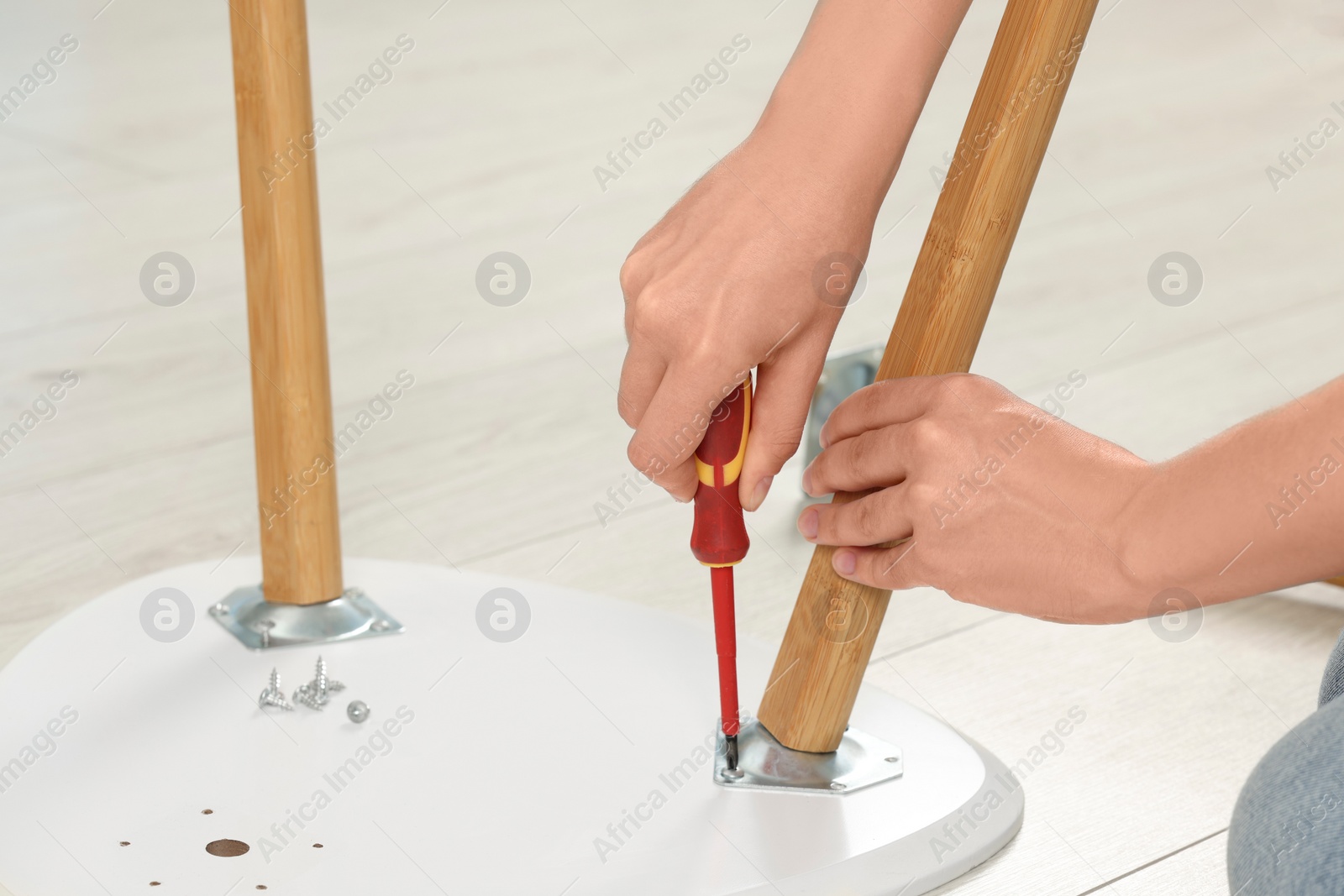 Photo of Woman with screwdriver assembling furniture on floor, closeup