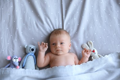 Cute newborn baby with toys in bed, top view