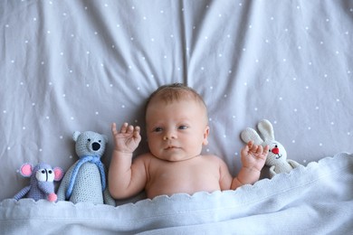 Photo of Cute newborn baby with toys in bed, top view