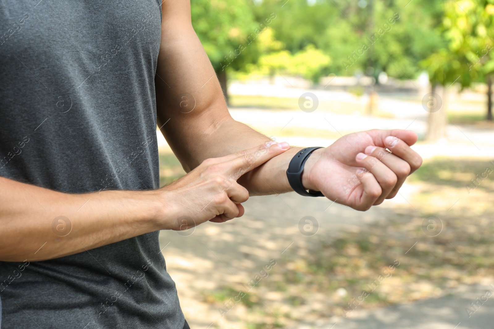 Photo of Young man checking pulse after training outdoors, closeup