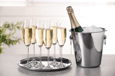 Photo of Glasses with champagne and bottle in bucket on table indoors