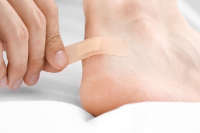 Photo of Man applying adhesive bandage on heel indoors, closeup