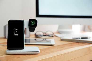 Photo of Mobile phone and smartwatch with wireless charger on wooden table. Modern workplace accessory