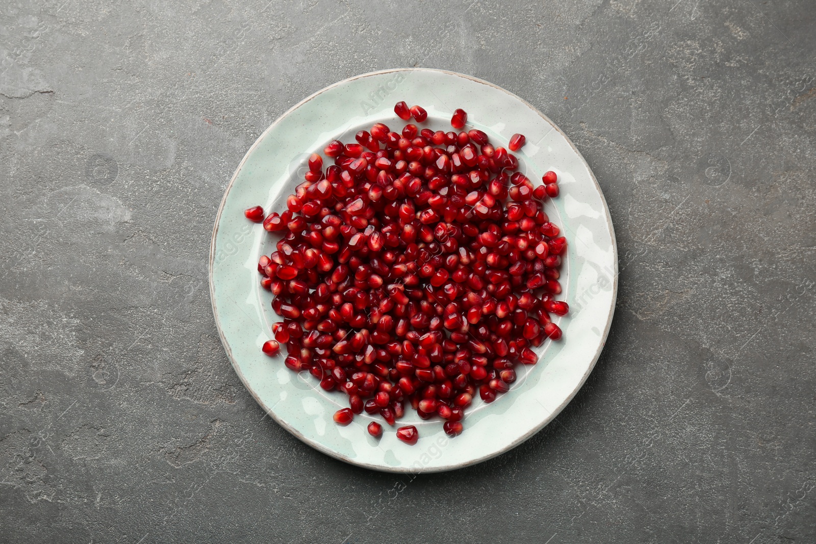 Photo of Tasty ripe pomegranate grains on grey table, top view