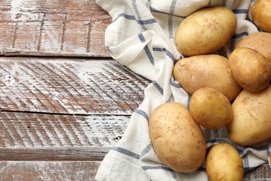 Photo of Raw fresh potatoes and napkin on wooden table, top view. Space for text