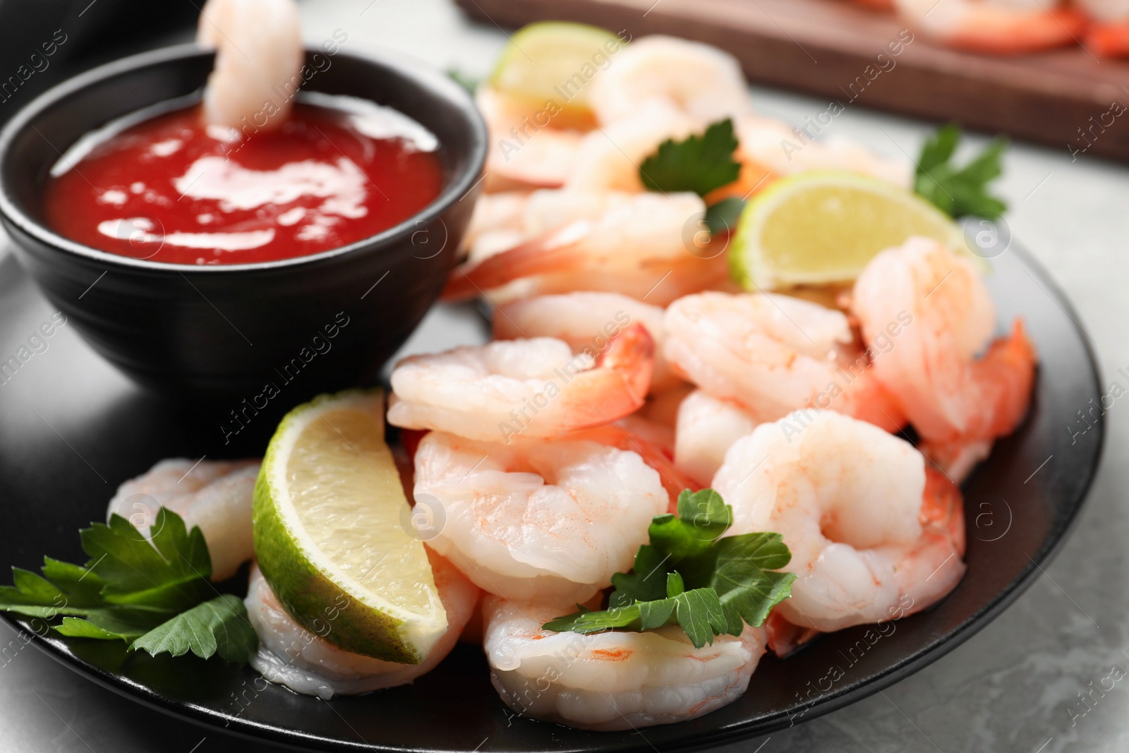 Photo of Tasty boiled shrimps with cocktail sauce, parsley and lime on light grey table, closeup