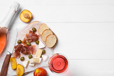 Delicious rose wine and snacks on white wooden table, flat lay. Space for text