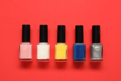 Photo of Bright nail polishes in bottles on red background, flat lay