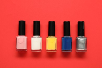 Bright nail polishes in bottles on red background, flat lay