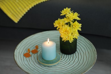 Photo of Side table with candle, flowers and earrings near sofa in room, closeup. Interior design