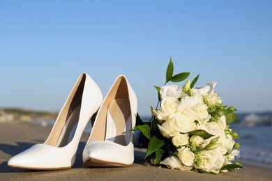 Photo of Beautiful wedding bouquet and shoes on sandy beach