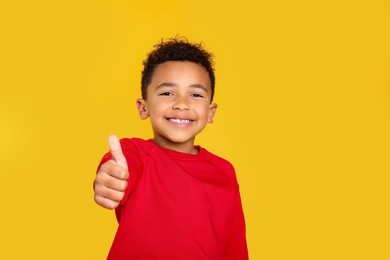 African-American boy showing thumb up on yellow background. Space for text