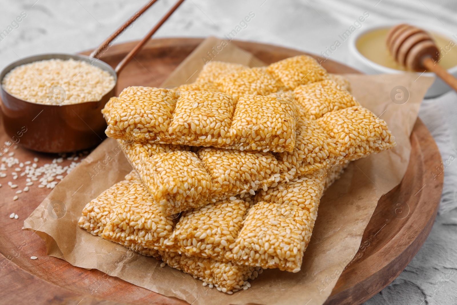 Photo of Wooden tray with delicious sweet kozinaki bars and sesame seeds on white table, closeup