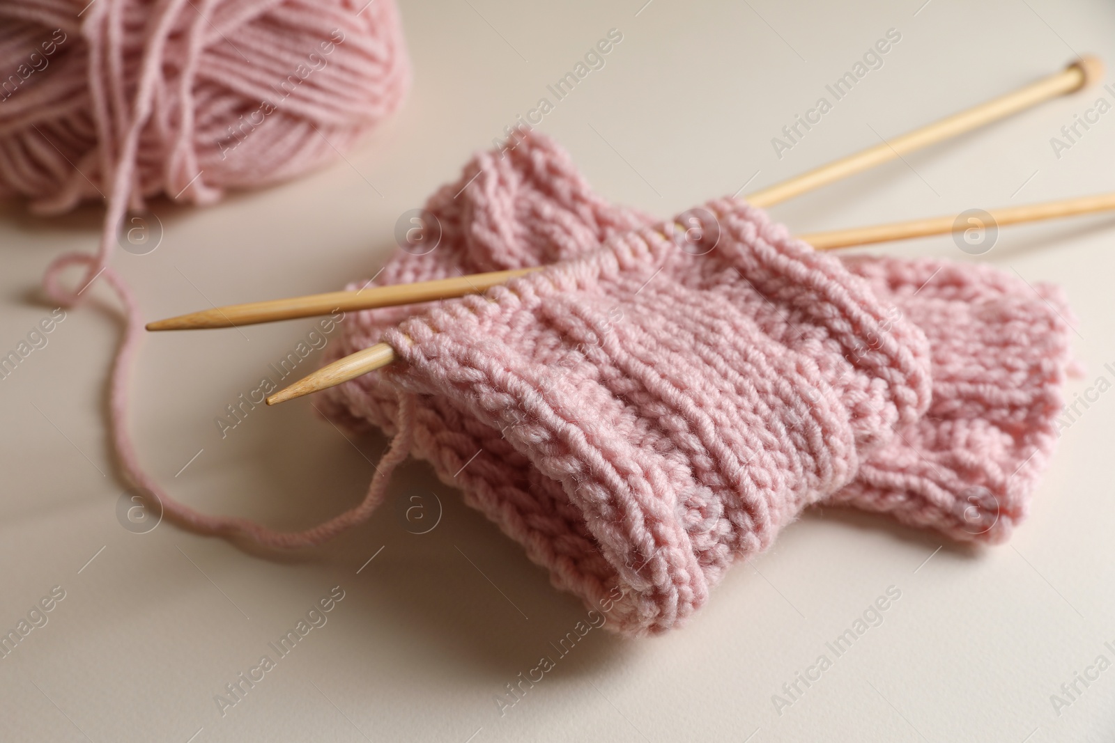 Photo of Pink knitting and needles on beige background, closeup