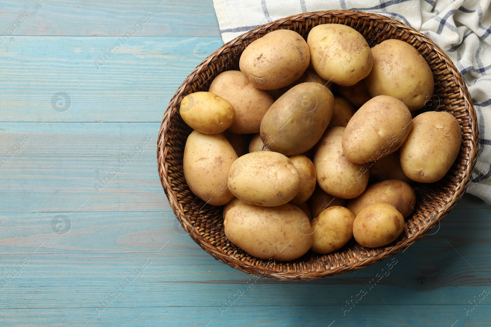 Photo of Raw fresh potatoes in wicker basket on light blue wooden table, top view. Space for text