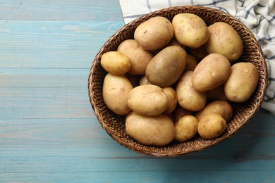 Photo of Raw fresh potatoes in wicker basket on light blue wooden table, top view. Space for text