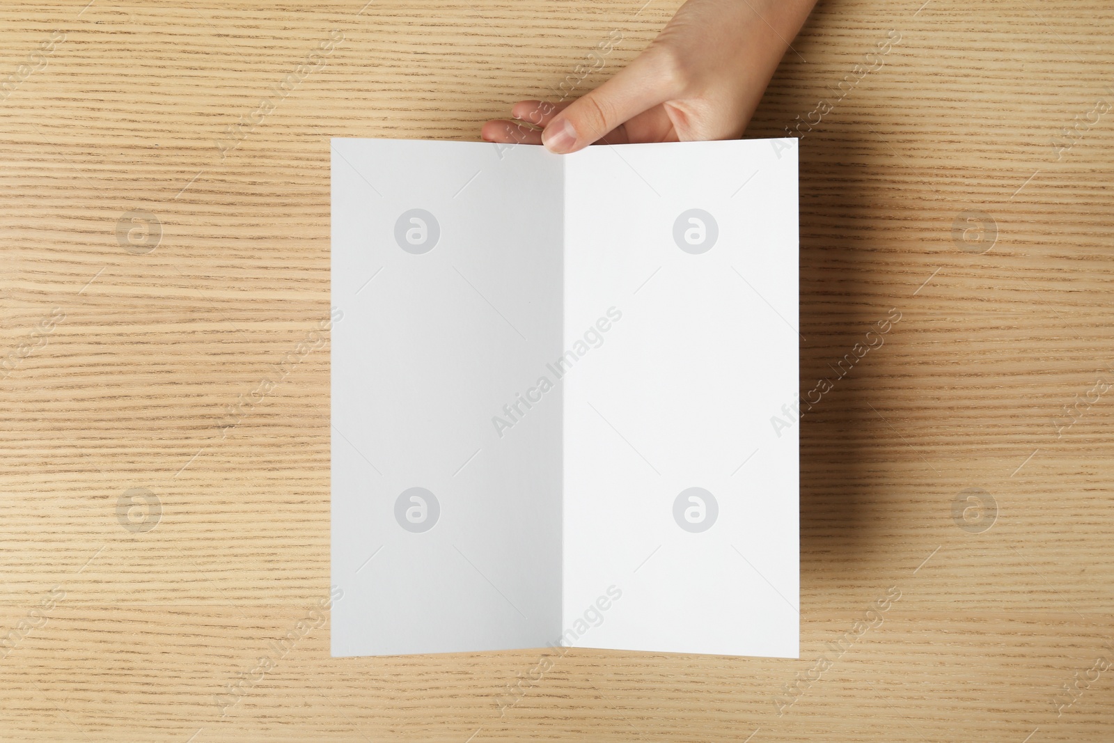 Photo of Woman holding blank brochure mock up on wooden table, top view