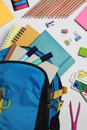 Backpack with different school stationery on white background, flat lay