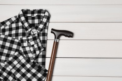 Photo of Elegant walking cane and checkered shirt on white wooden table, flat lay. Space for text