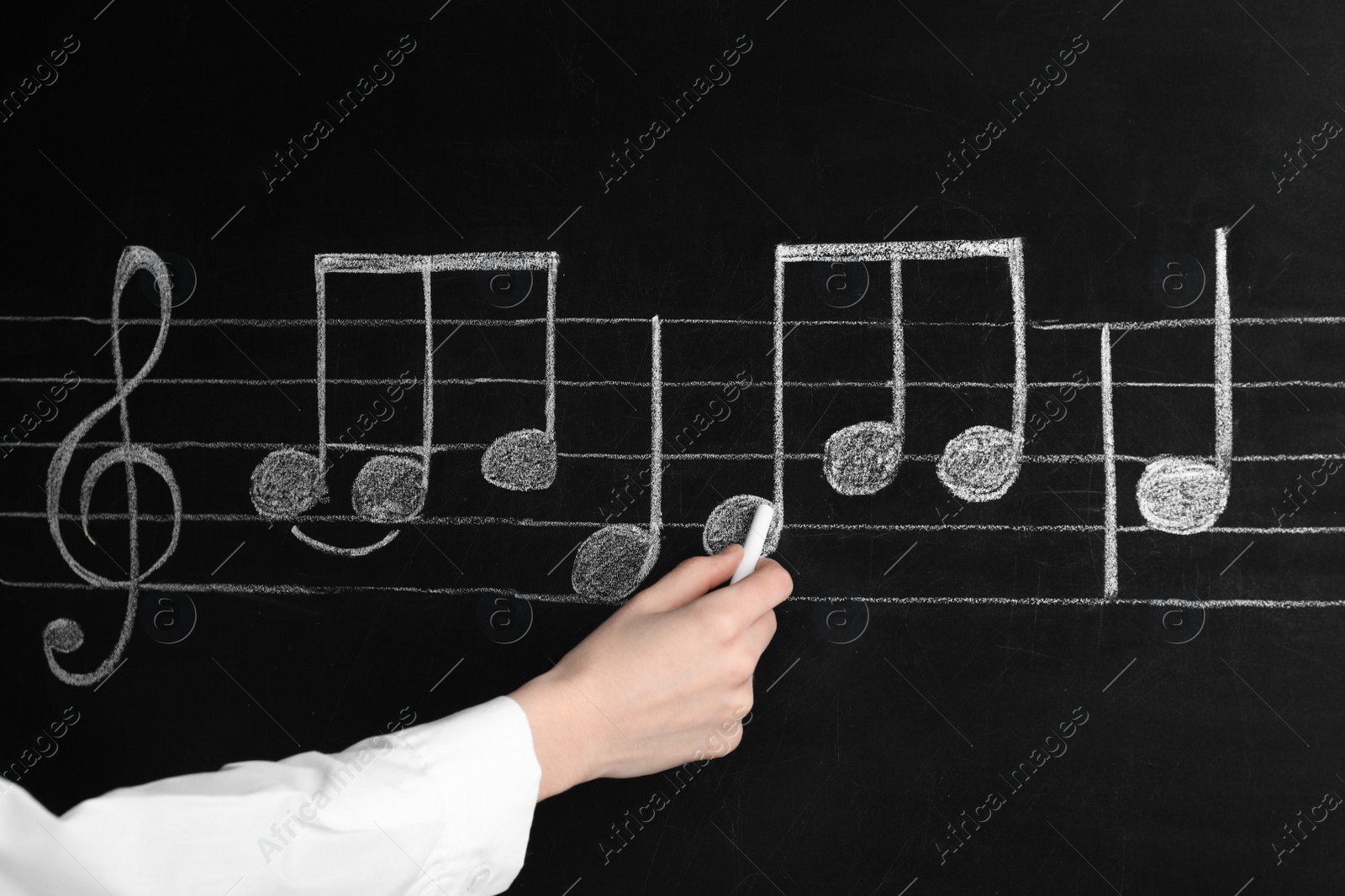 Photo of Woman writing music notes with chalk on blackboard, closeup