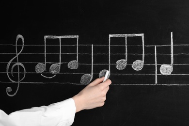 Woman writing music notes with chalk on blackboard, closeup