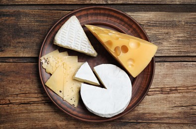 Clay plate with different cheeses on wooden table, top view
