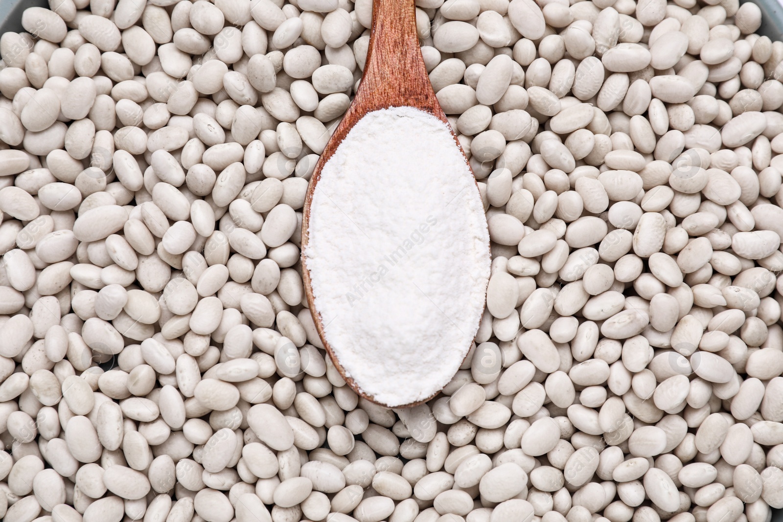 Photo of Wooden spoon with flour on white kidney beans, top view