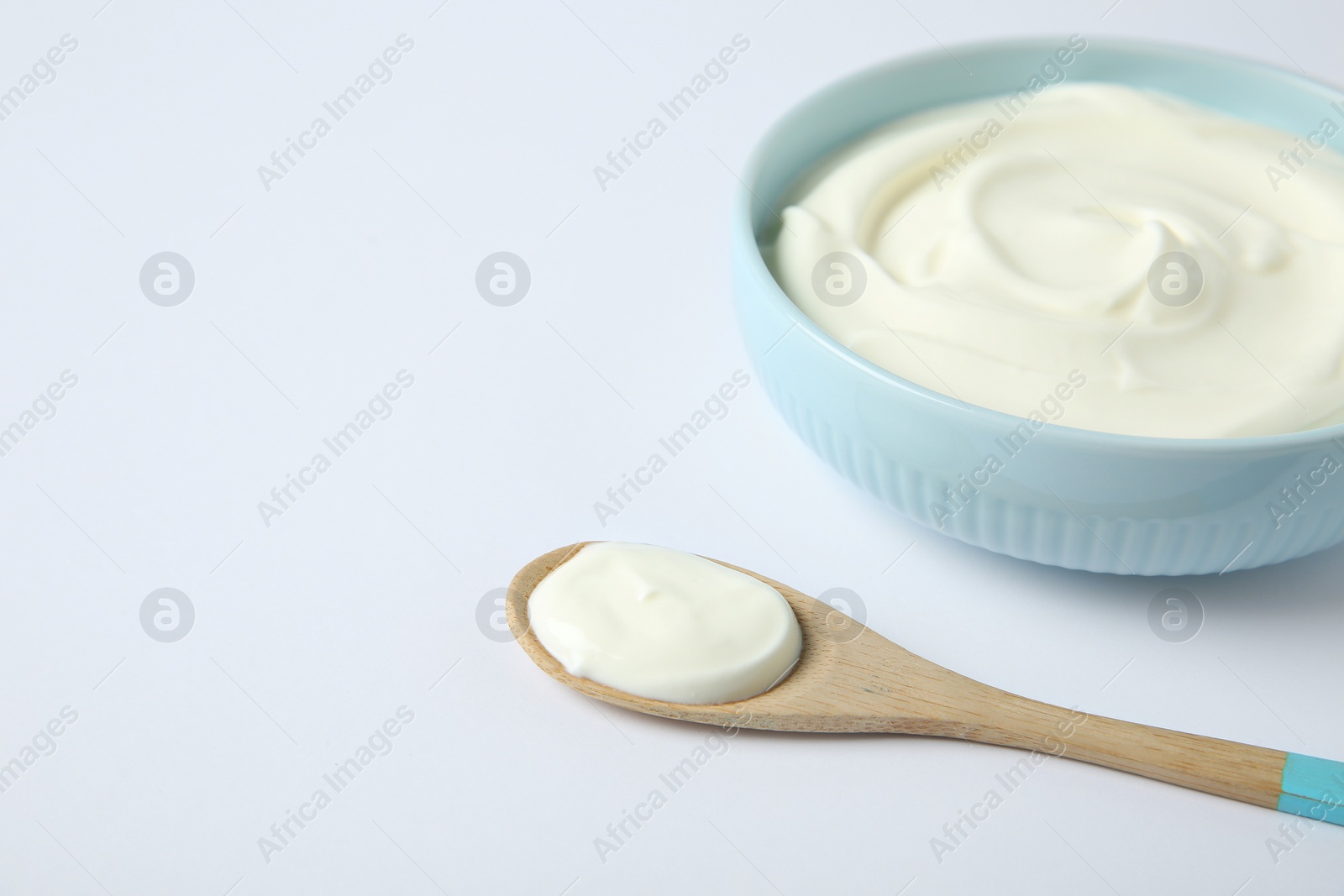 Photo of Bowl of sour cream and wooden spoon on white background