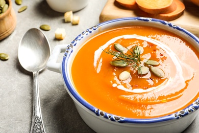 Photo of Bowl of tasty sweet potato soup and spoon on table, closeup