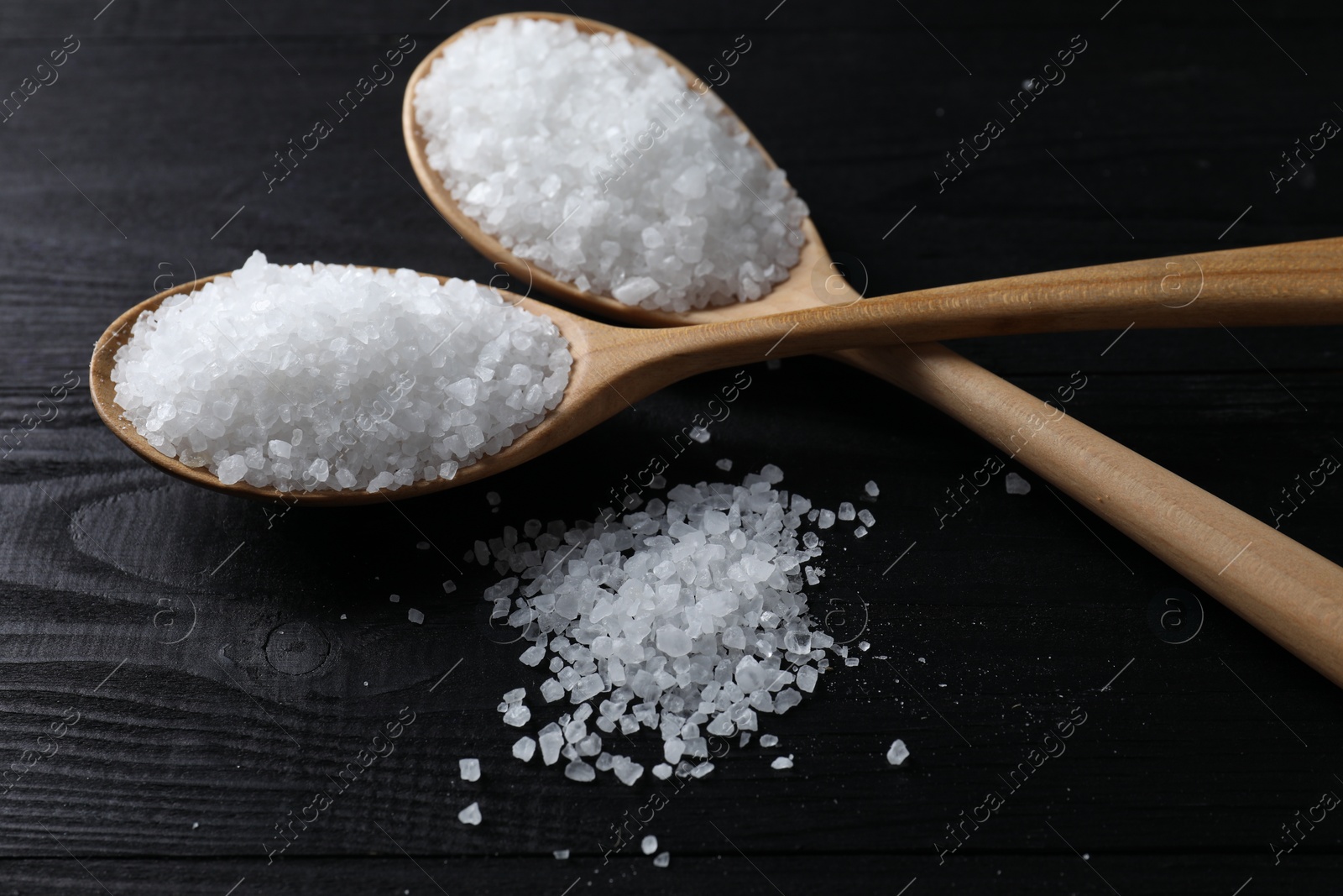 Photo of Organic salt in spoons on black wooden table, closeup