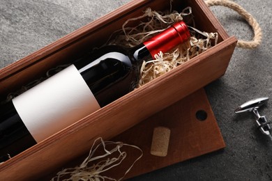 Bottle of wine in wooden box, cork and corkscrew on dark textured table, above view