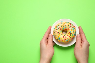 Woman holding plate with delicious glazed donut on green background, top view. Space for text