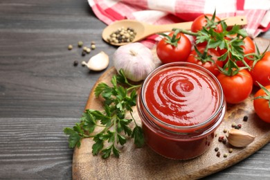 Photo of Tasty ketchup, fresh tomatoes, parsley and spices on grey wooden table, space for text