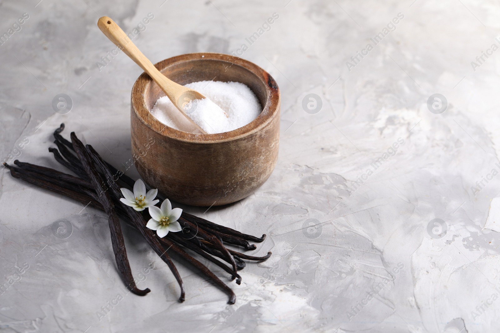 Photo of Vanilla pods, flowers and bowl with sugar on light textured table, closeup. Space for text