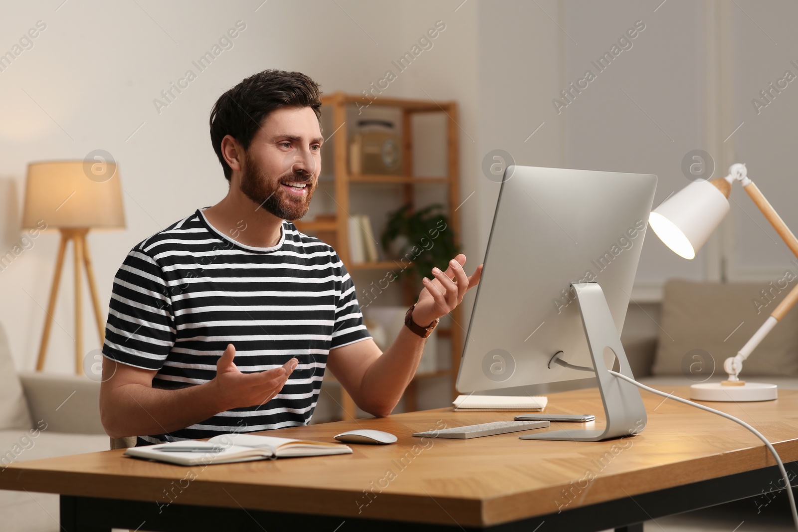 Photo of Home workplace. Happy man having video conference at wooden desk in room