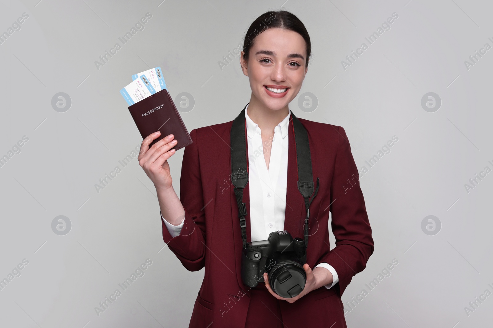 Photo of Smiling businesswoman with passport, tickets and camera on grey background