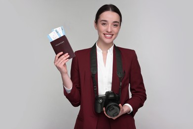 Photo of Smiling businesswoman with passport, tickets and camera on grey background