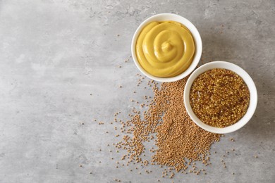 Bowls with mustard and seeds on grey table, flat lay. Space for text