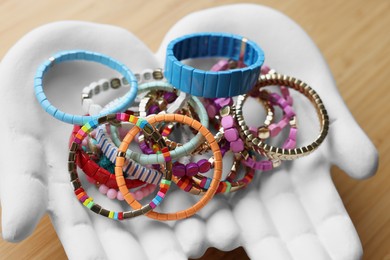 Ceramic hand stand with many stylish bracelets on wooden table, closeup