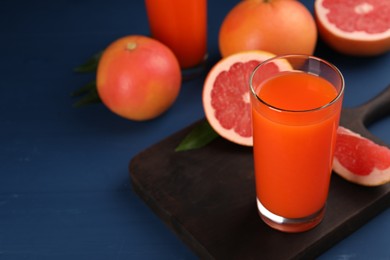 Photo of Tasty grapefruit juice in glass and fresh fruits on blue wooden table. Space for text