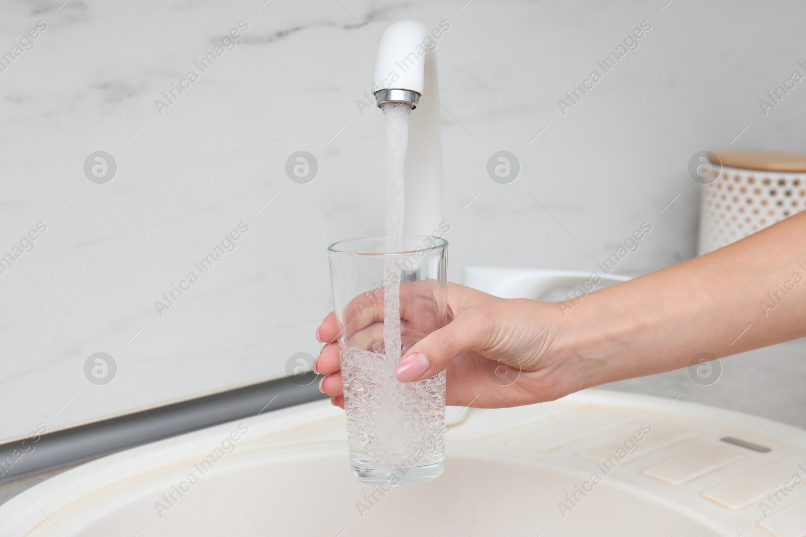 Photo of Woman filling glass with water from faucet in kitchen, closeup