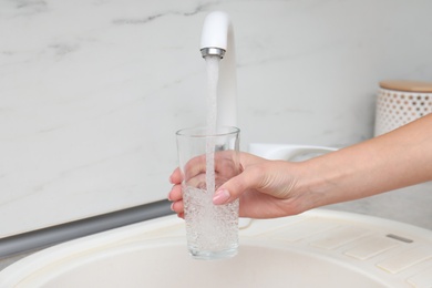 Photo of Woman filling glass with water from faucet in kitchen, closeup