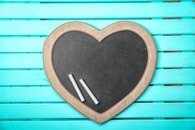 Photo of Empty heart shaped blackboard with chalk on wooden background