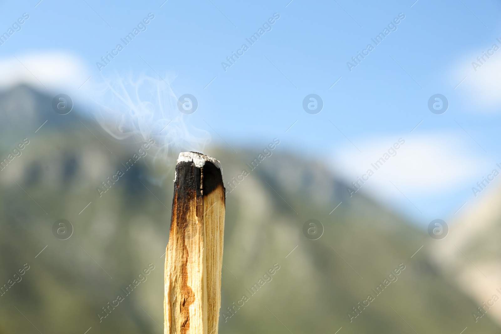 Photo of Burning palo santo stick in high mountains, closeup. Space for text