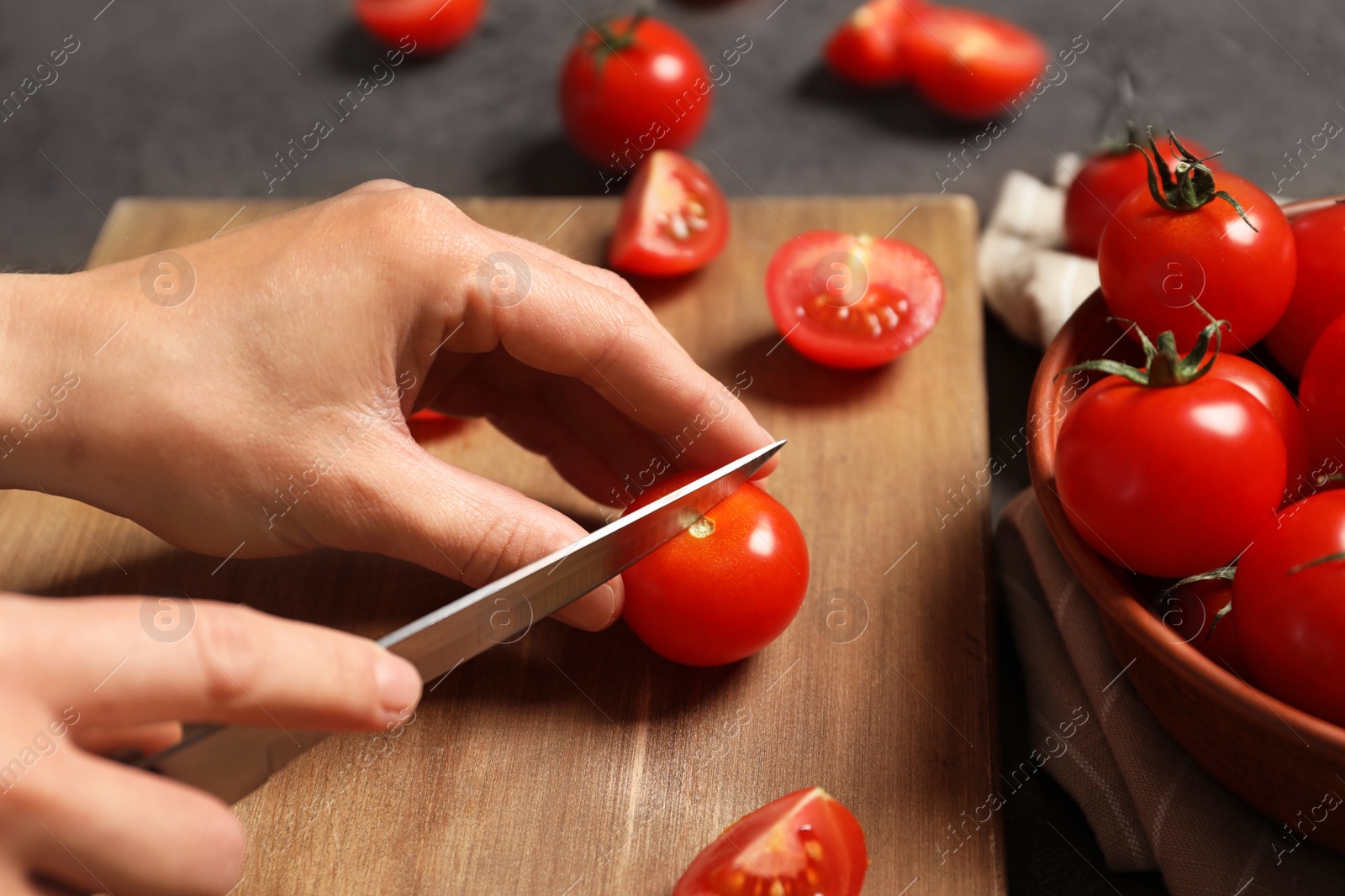 Photo of Woman cutting fresh cherry tomatoes on wooden board at table, closeup