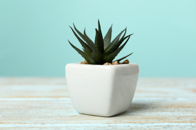 Artificial plant in white flower pot on light blue wooden table