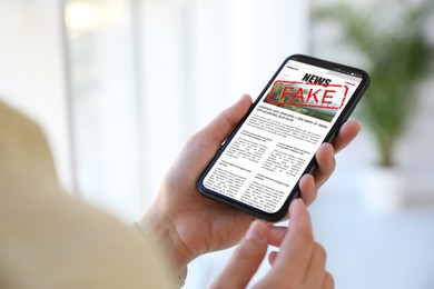 Image of Fake information. Woman using mobile phone to read news at home, closeup